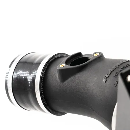 Close-up van de RamAir Proram inlaatkit voor de Toyota GR Yaris. De kit bestaat uit een zwart inlaatspruitstuk met zilveren klemmen en een connector. Op de achtergrond is een witte, neutrale achtergrond te zien.