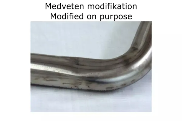 Close-up van een gebogen RVS-buis voor een Simons sportuitlaatsysteem. De pijp is glanzend zilver met lichte slijtage. Boven de pijp staat: Medveten modification Modified on purpose. Onderdeel voor BMW F30 320i, 328i.